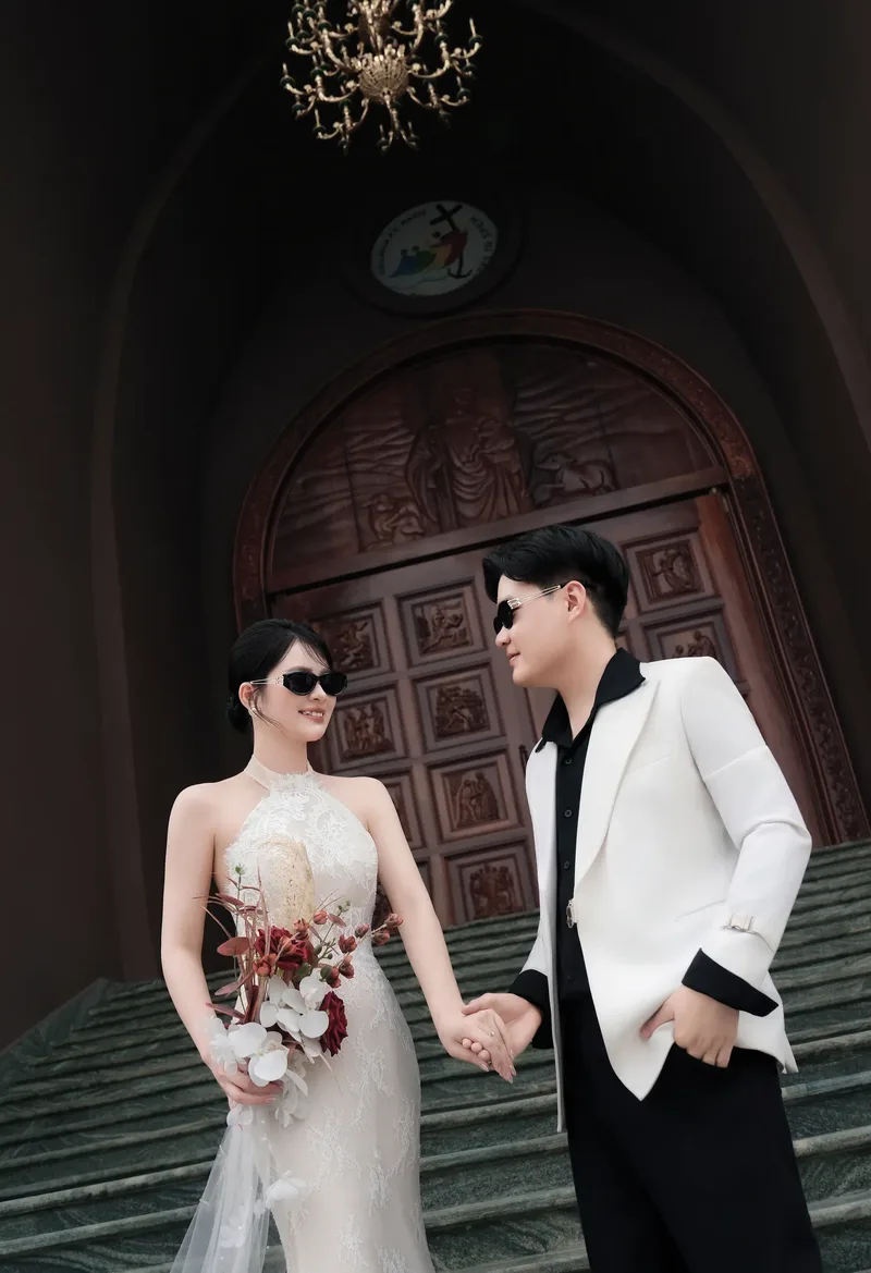 Cô dâu chú rể nắm tay trước cánh cửa gỗ nhà thờ